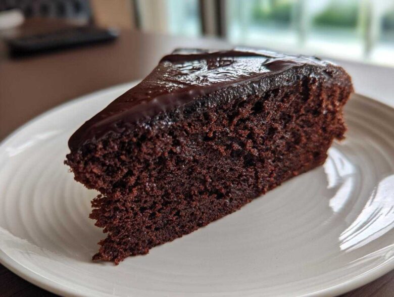 A moist slice of rich Gluten-Free Chocolate Cake topped with glossy dark chocolate ganache on a white plate.