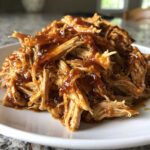 A mound of shredded Slow Cooker Honey Garlic Pulled Pork glistening with a thick, sweet sauce on a white plate.
