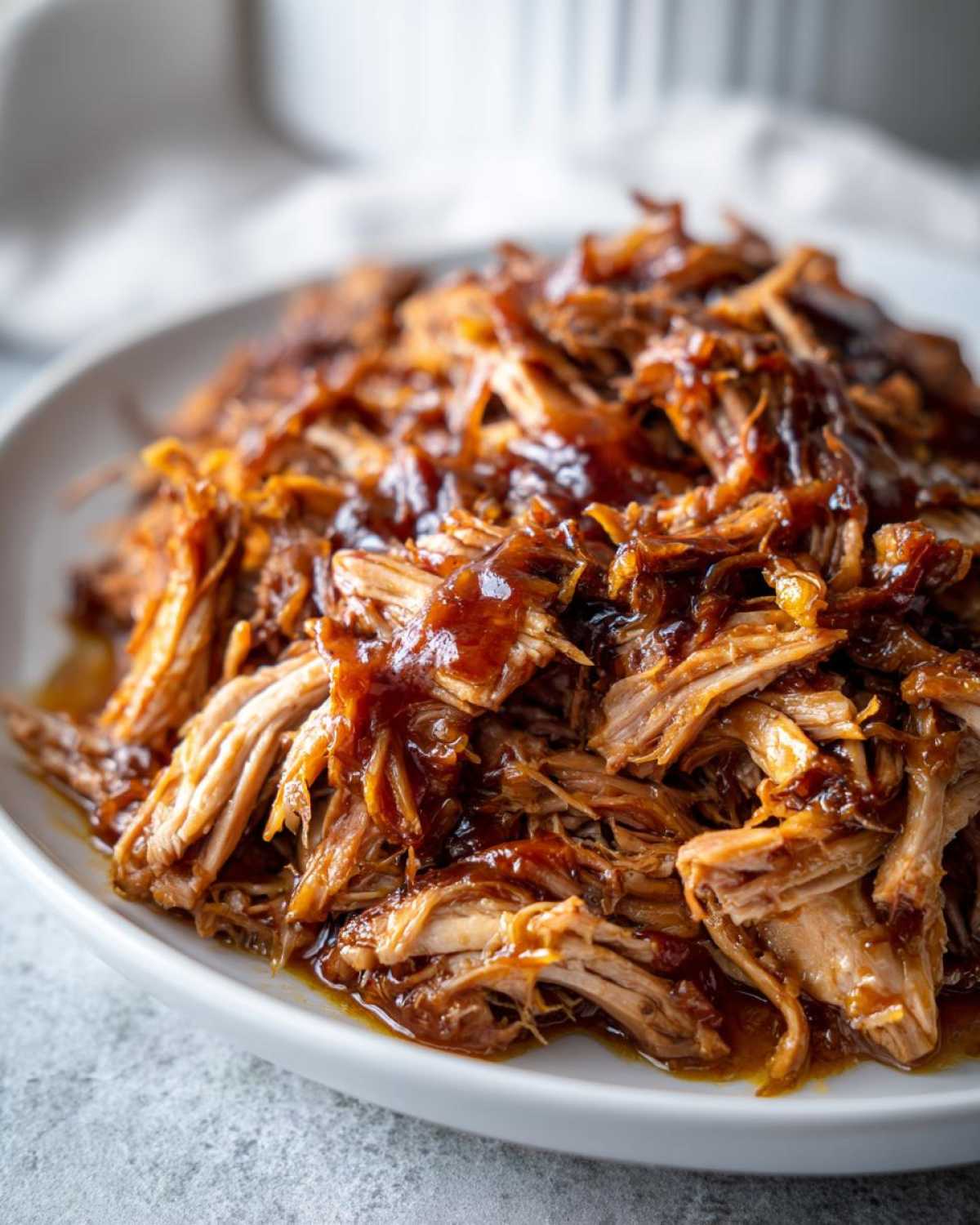 Close-up of tender, shredded Slow Cooker Honey Garlic Pulled Pork coated in a rich, glossy sauce on a white plate.