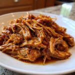 A close-up of shredded Slow Cooker Honey Garlic Pulled Pork coated in a glossy sauce on a white plate.