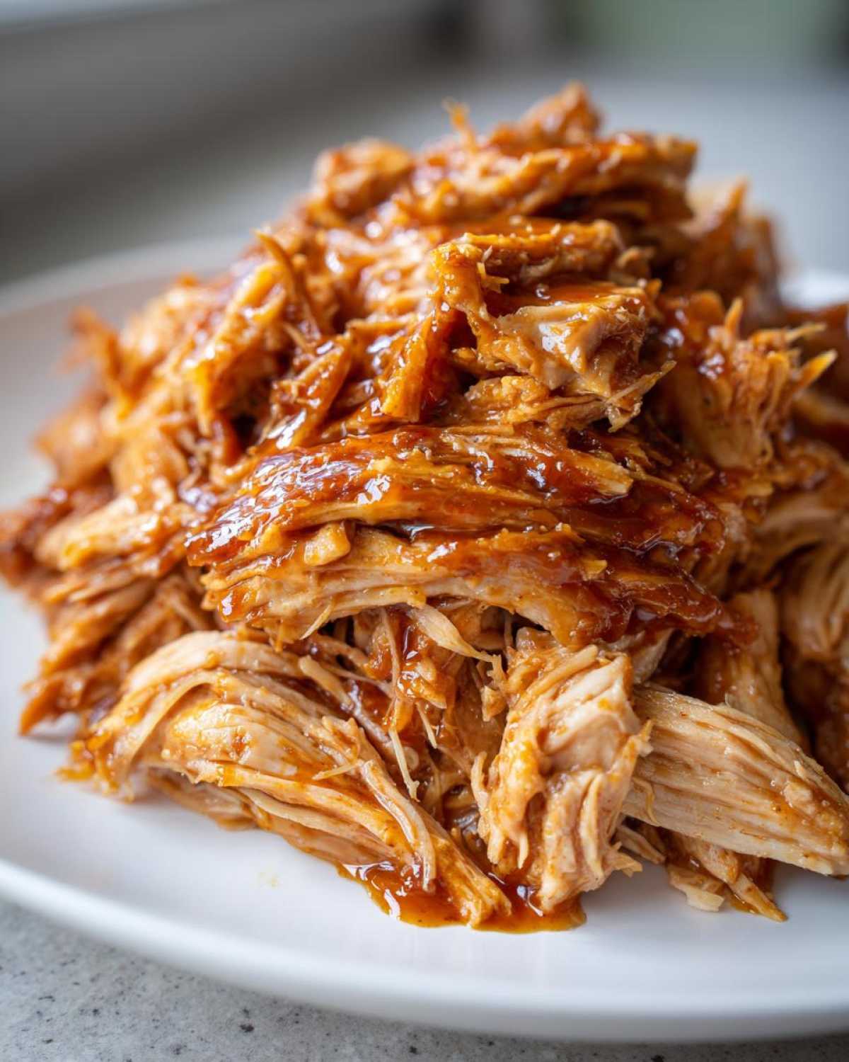 Close-up of tender, shredded Slow Cooker Honey Garlic Pulled Pork coated in a glossy, rich sauce on a white plate.