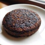Close-up of a dark, well-seared Smoky Black Bean Burger Patty resting on a white plate.