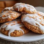 A stack of Soft-Baked Carrot Cake Cookies with Cream Cheese Glaze drizzled on top and sprinkled with carrot zest.
