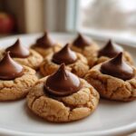 Close-up of several soft Peanut Butter Blossom Cookies arranged on a white plate, each topped with a melted chocolate kiss.