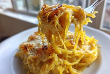Close-up of cheesy Spaghetti Squash Alfredo strands being lifted high on a fork from a serving on a white plate.