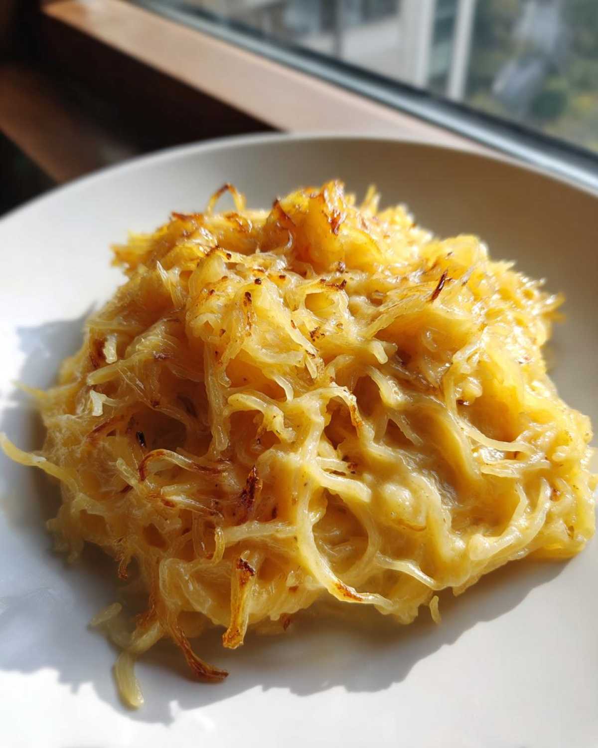 A close-up shot of a serving of creamy Spaghetti Squash Alfredo on a white plate, showing golden strands.
