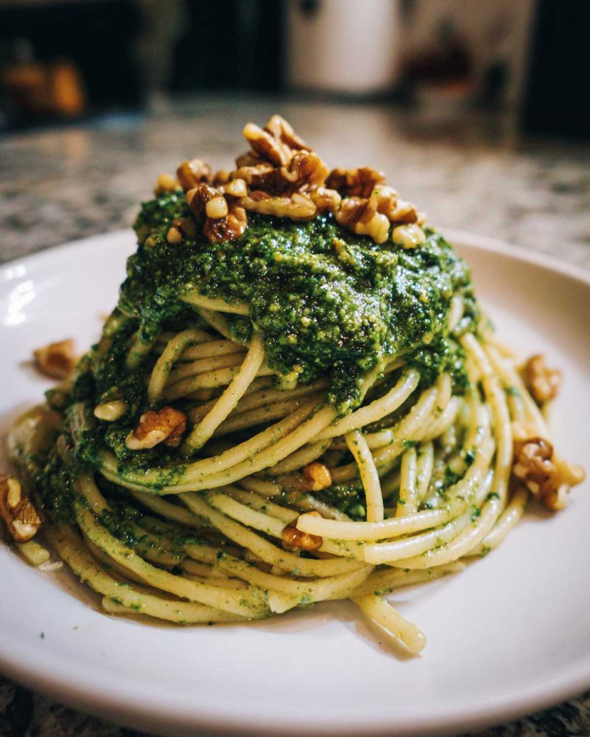 A mound of spaghetti generously topped with bright green Vegan Basil Pesto and whole walnuts.