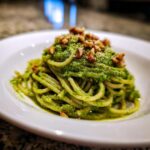 Close-up of spaghetti coated in bright green Vegan Basil Pesto, topped with chopped walnuts.