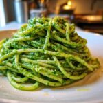 A mound of spaghetti generously coated in bright green Vegan Basil Pesto, served on a white plate.