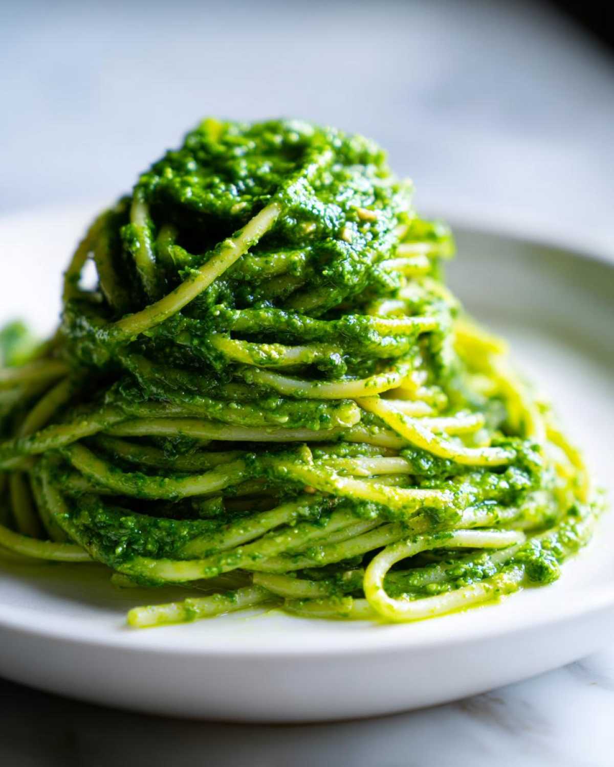 A mound of spaghetti generously coated with vibrant green Vegan Basil Pesto on a white plate.