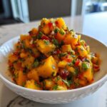Close-up of a white bowl overflowing with fresh Spicy Mango Salsa, featuring diced mango, red chili, and cilantro.