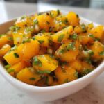 Close-up of vibrant, chunky Spicy Mango Salsa featuring diced mango, cilantro, and chili flakes in a small white bowl.