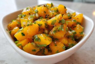 Close-up of vibrant, chunky Spicy Mango Salsa featuring diced mango, cilantro, and chili flakes in a small white bowl.