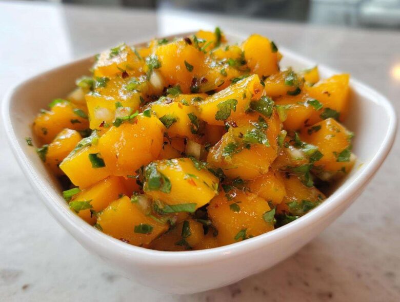 Close-up of vibrant, chunky Spicy Mango Salsa featuring diced mango, cilantro, and chili flakes in a small white bowl.