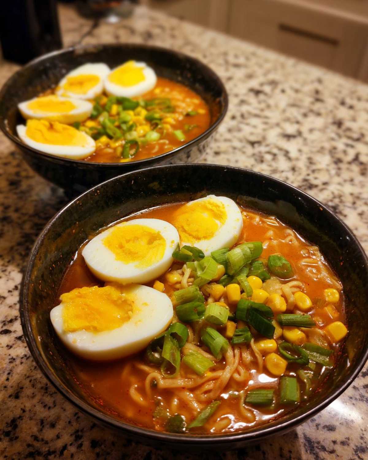 Two bowls of Spicy Miso Ramen with soft-boiled eggs, corn, and green onions on a granite counter.