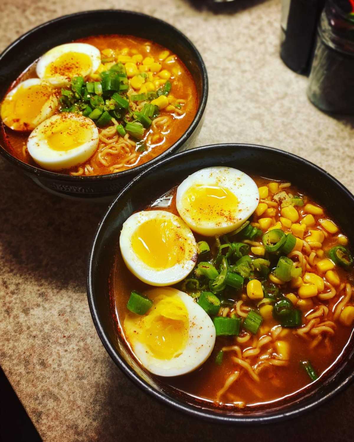 Two bowls of Spicy Miso Ramen featuring noodles, corn, green onions, and halved soft-boiled eggs.