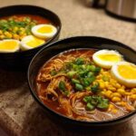 Two bowls of Spicy Miso Ramen featuring shredded chicken, corn, green onions, and soft-boiled eggs.