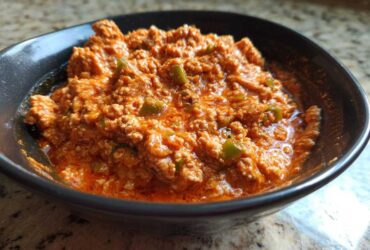 Close-up of a rich, orange-red serving of Spicy Turkey White Bean Chili with visible ground turkey and green peppers in a dark bowl.