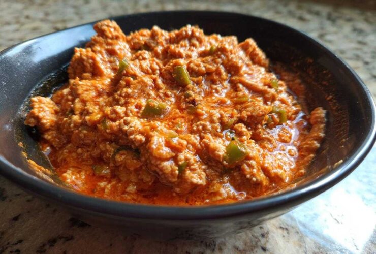 Close-up of a rich, orange-red serving of Spicy Turkey White Bean Chili with visible ground turkey and green peppers in a dark bowl.