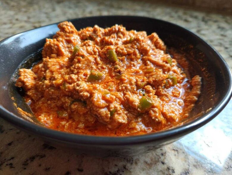 Close-up of a rich, orange-red serving of Spicy Turkey White Bean Chili with visible ground turkey and green peppers in a dark bowl.