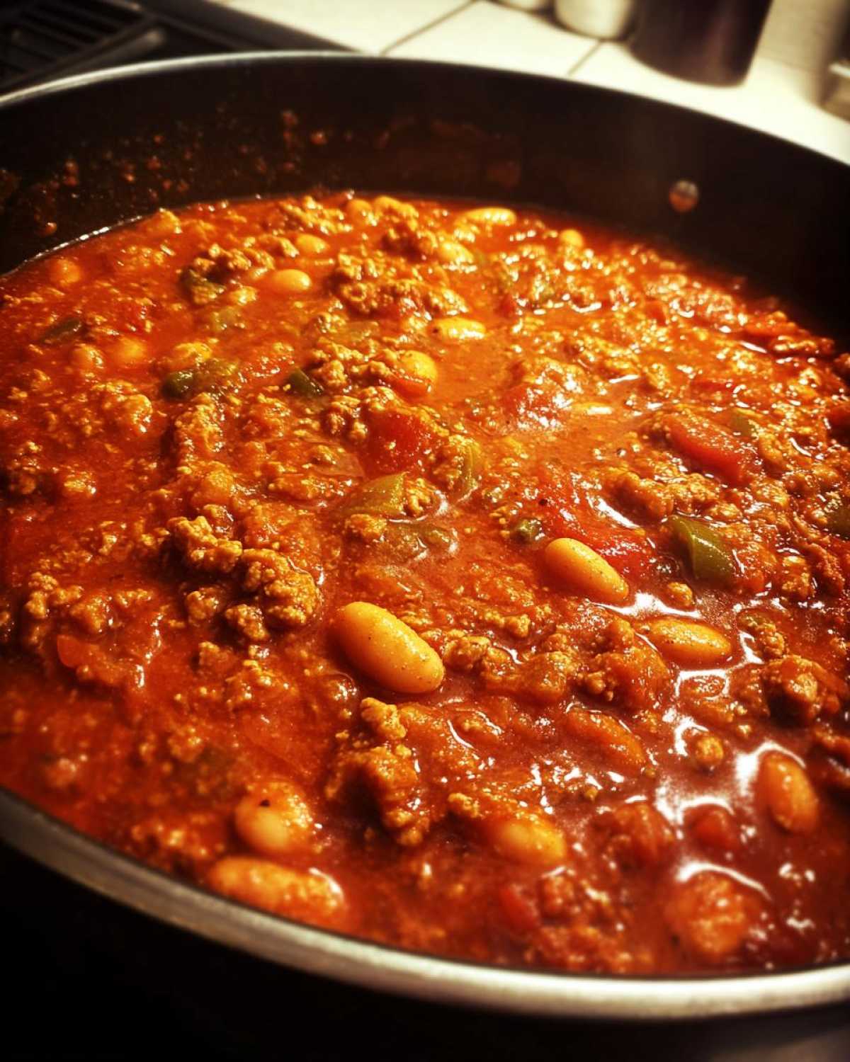 Close-up of rich, red Spicy Turkey White Bean Chili simmering in a dark pot, showing ground turkey and white beans.