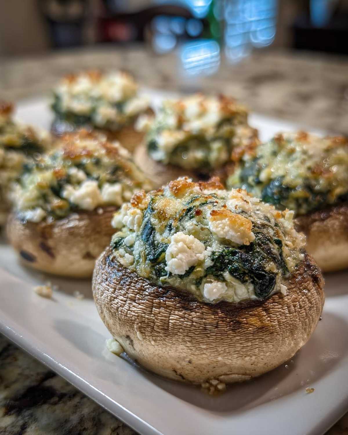 A close-up of baked Spinach and Feta Stuffed Mushrooms piled high with cheesy filling on a white platter.