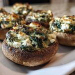 Close-up of baked Spinach and Feta Stuffed Mushrooms with golden-brown tops on a white serving platter.
