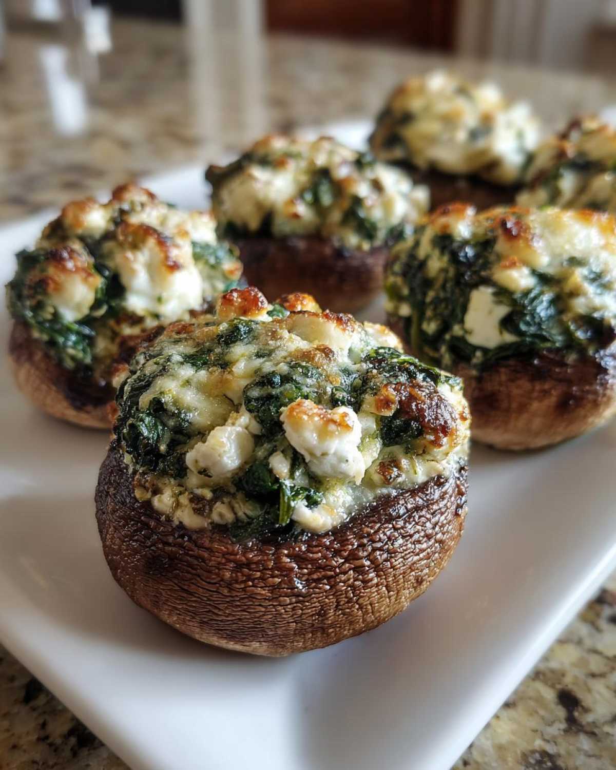 Close-up of baked Spinach and Feta Stuffed Mushrooms with browned cheese topping on a white platter.