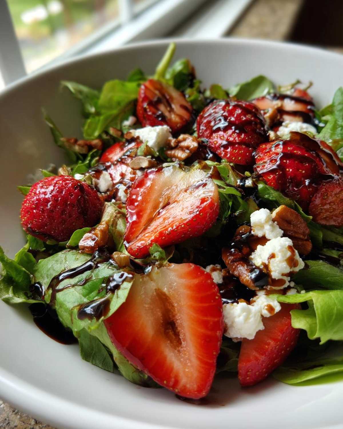 Close-up of a vibrant Spring Mix Salad with Strawberries and Goat Cheese, drizzled with balsamic glaze.