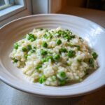 A close-up of creamy Spring Pea and Mint Risotto served in a white bowl, topped with fresh mint.