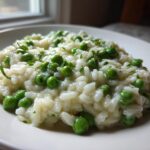 A close-up of creamy Spring Pea and Mint Risotto served on a white plate, garnished with bright green peas and mint.