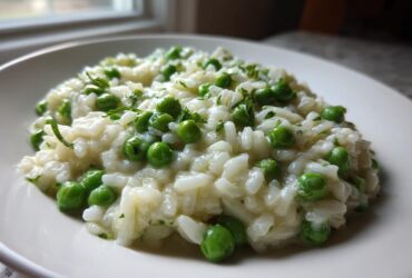 A close-up of creamy Spring Pea and Mint Risotto served on a white plate, garnished with bright green peas and mint.
