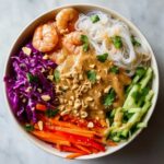 Overhead view of a vibrant Spring Roll Bowl with Peanut Sauce, featuring shrimp, rice noodles, and colorful shredded vegetables.