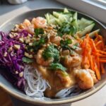 A colorful Spring Roll Bowl with Peanut Sauce featuring shrimp, rice noodles, shredded carrots, cucumber, and red cabbage.