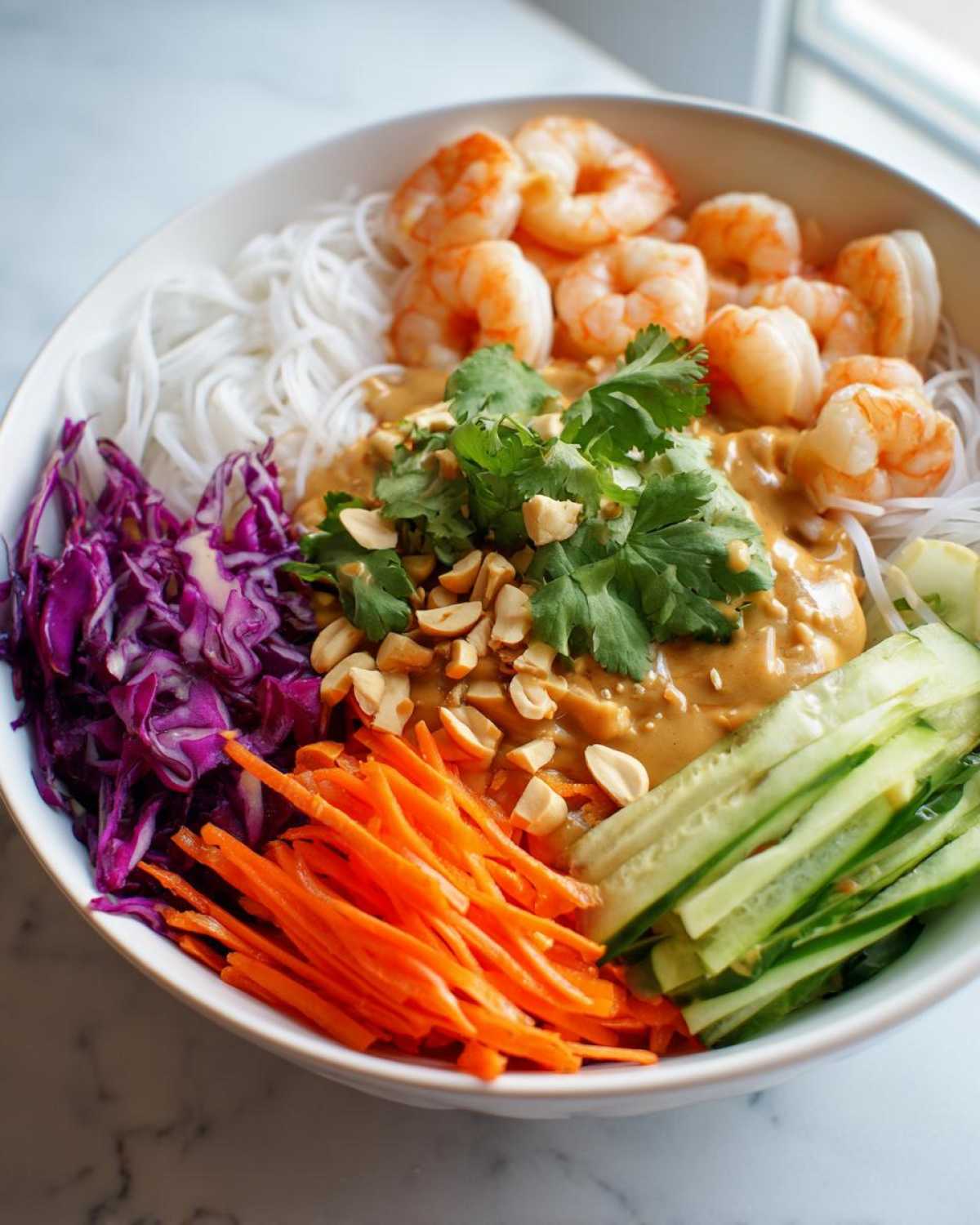 A vibrant Spring Roll Bowl with Peanut Sauce featuring rice noodles, shrimp, shredded carrots, cucumber, and red cabbage.