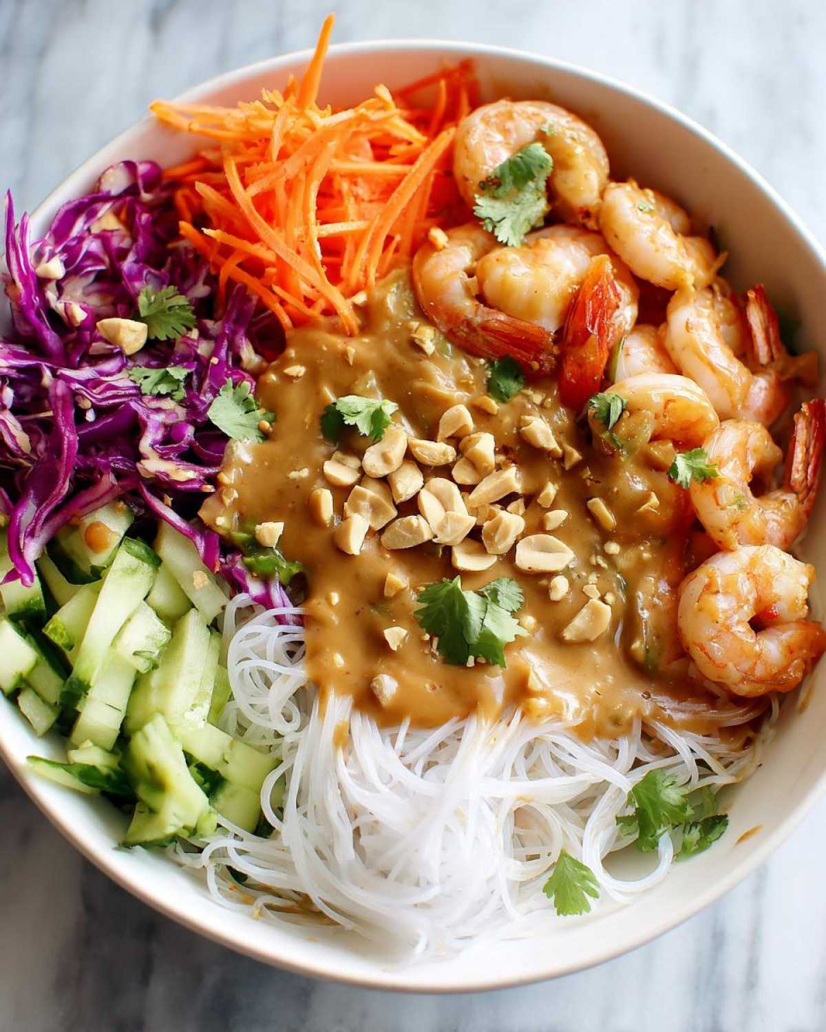 Overhead view of a Spring Roll Bowl with Peanut Sauce, featuring rice noodles, shrimp, shredded carrots, cucumber, and cabbage.