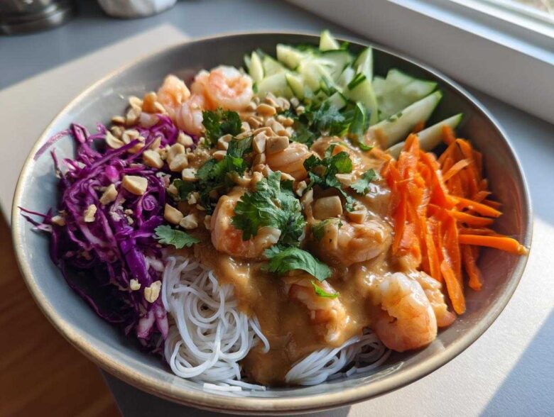 A colorful Spring Roll Bowl with Peanut Sauce featuring shrimp, rice noodles, shredded carrots, cucumber, and red cabbage.