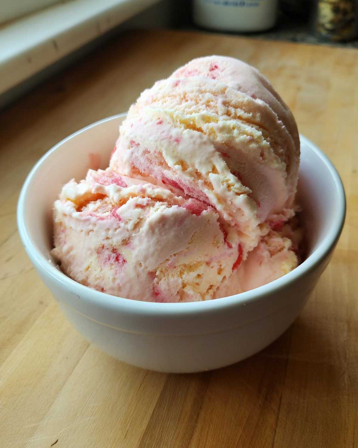 Two scoops of pink and white swirled Strawberry Banana Ice Cream served in a small white bowl.