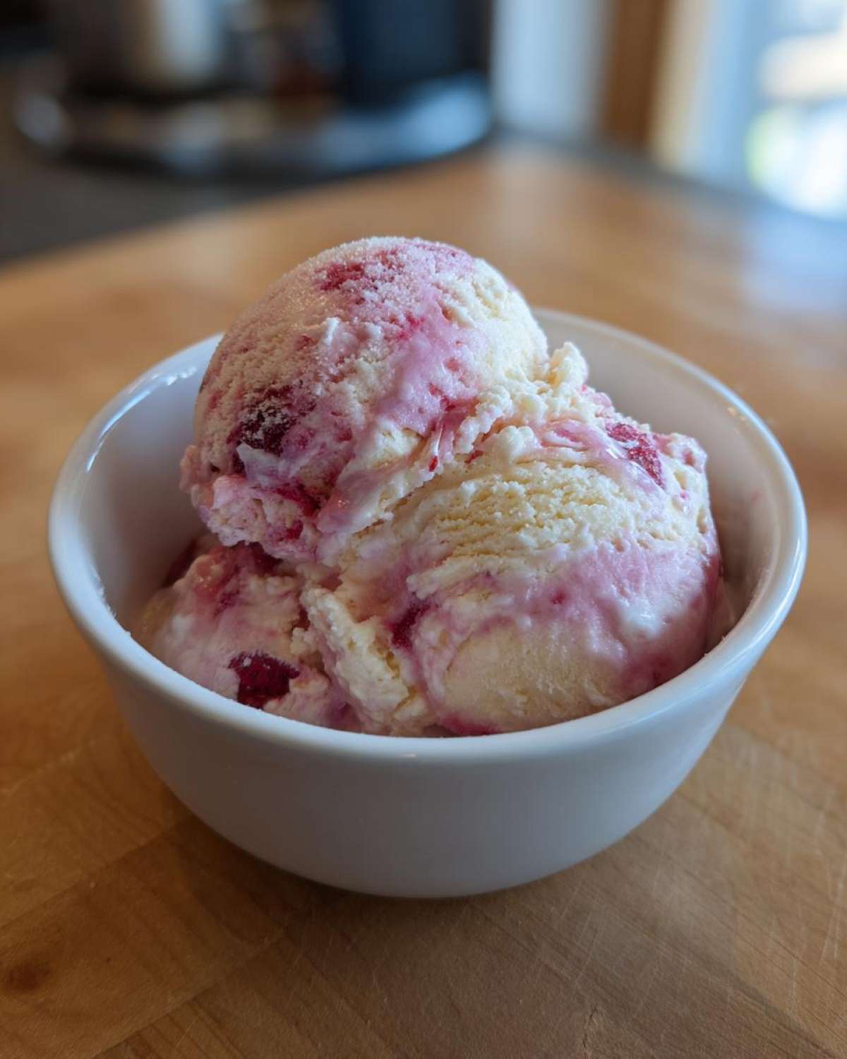 Two scoops of creamy Strawberry Banana Ice Cream swirled with bright pink fruit puree in a small white bowl.
