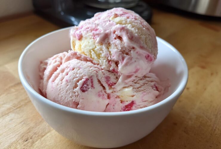 Two scoops of pink and white Strawberry Banana Ice Cream served in a small white bowl on a wooden surface.