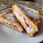 Two halves of golden Strawberry Cream Cheese Stuffed French Toast dusted with powdered sugar.