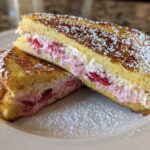 Two halves of Strawberry Cream Cheese Stuffed French Toast dusted with powdered sugar on a white plate.