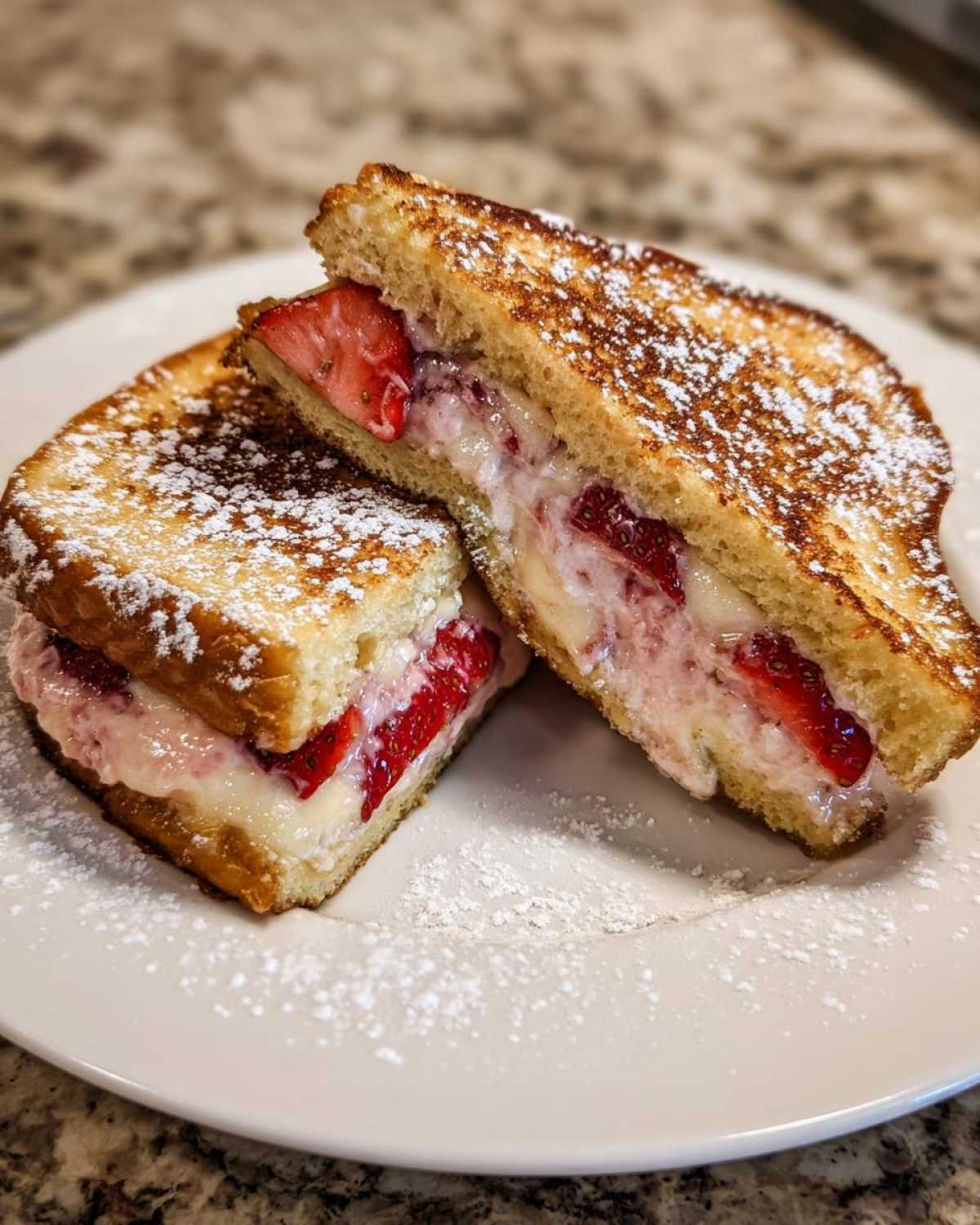 Two halves of Strawberry Cream Cheese Stuffed French Toast dusted with powdered sugar on a white plate.