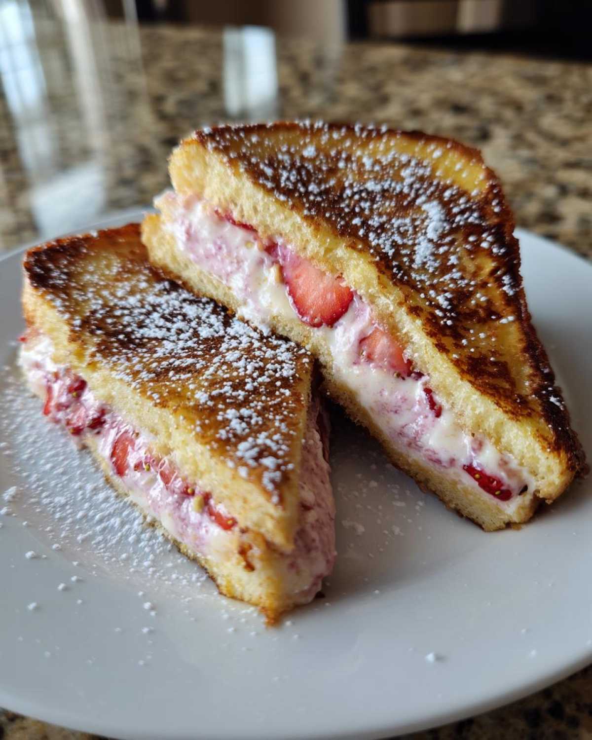Two halves of Strawberry Cream Cheese Stuffed French Toast dusted with powdered sugar on a white plate.
