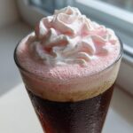 Close-up of a glass of Strawberry Cream Cold Brew topped with pink foam and whipped cream.