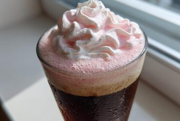 Close-up of a glass of Strawberry Cream Cold Brew topped with pink foam and whipped cream.