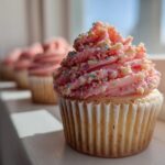 A close-up of a single Strawberry Crunch Cupcakes featuring pink frosting topped with colorful sprinkles and crunch pieces.