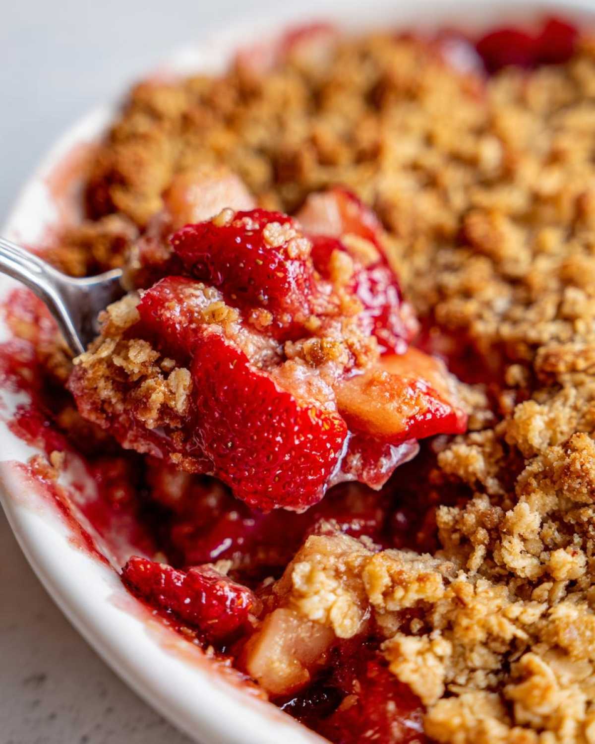 A spoonful of warm Strawberry Rhubarb Crisp showing juicy strawberries and crunchy oat topping.