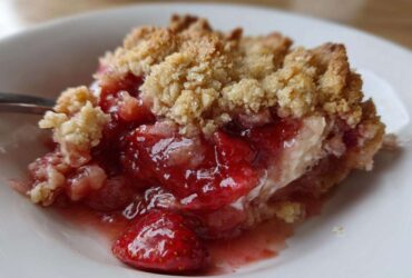 Close-up of a serving of warm Strawberry Rhubarb Crisp showing juicy fruit filling and golden crumble topping.