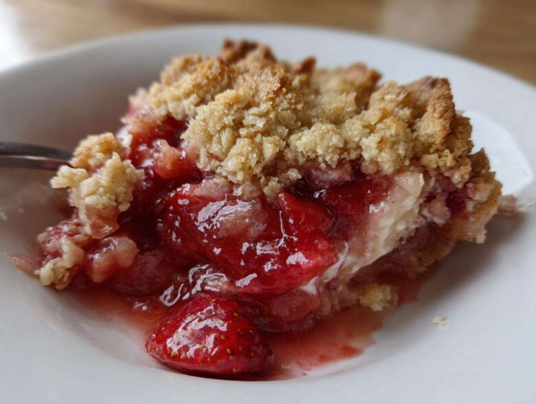 Close-up of a serving of warm Strawberry Rhubarb Crisp showing juicy fruit filling and golden crumble topping.